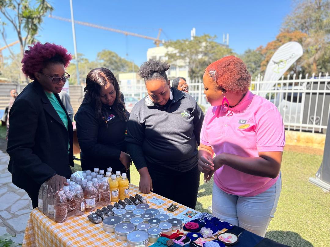 A woman sells juices, fabric and cosmetics to other women looking on