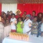 various women, some holding bottles of juice, standing in front of a table with bottles of juice