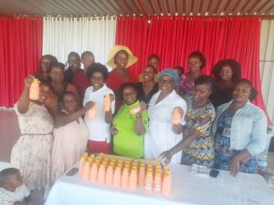 various women, some holding bottles of juice, standing in front of a table with bottles of juice