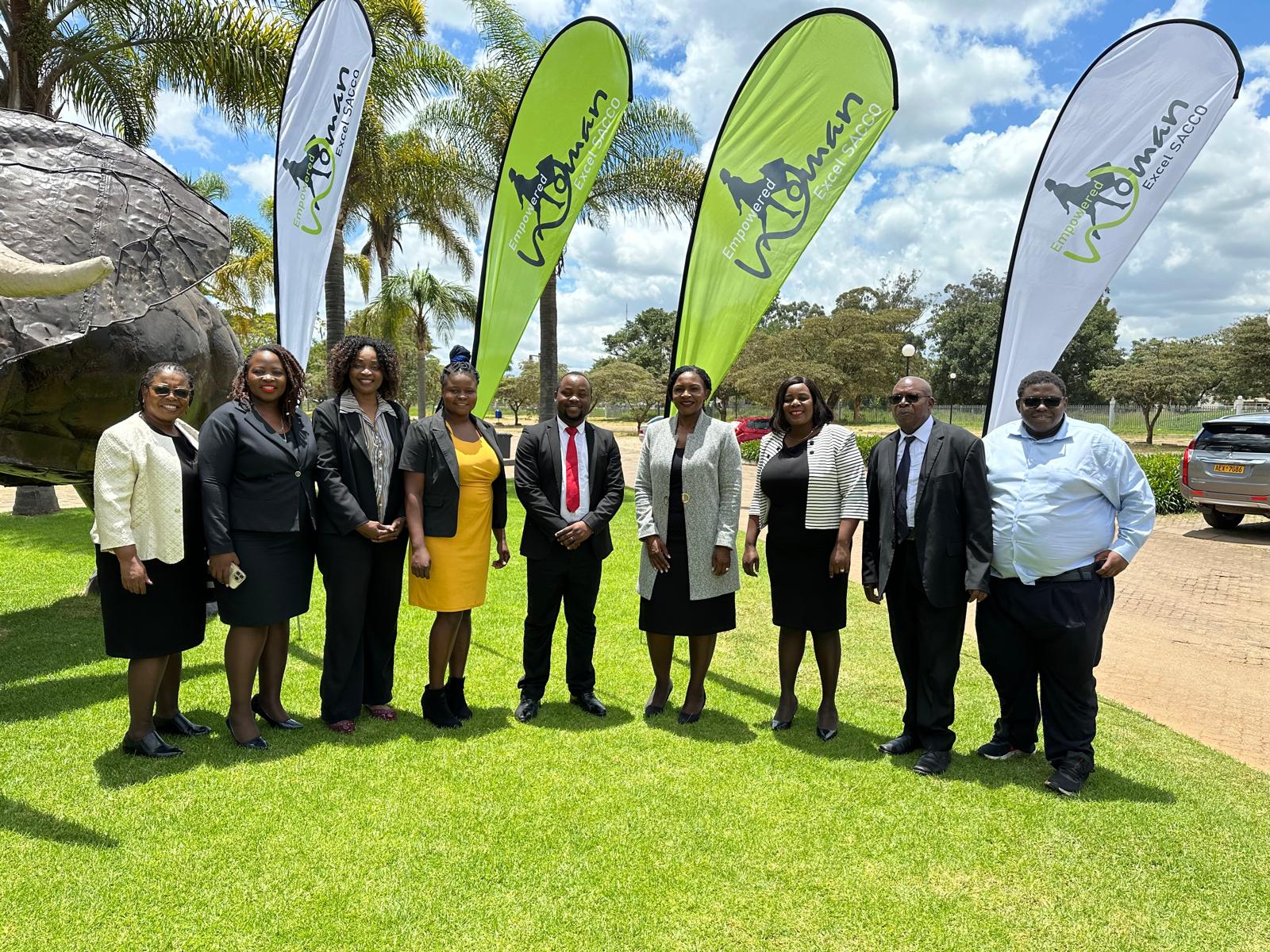 The SACCO Staff standing on greass in front of SACCO banners, ready to serve you.